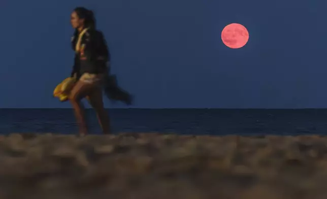 A supermoon rises over the horizon of Lake Michigan as a person walks by in Milwaukee, Wis., Monday, Aug. 19, 2024. (John Hart/Wisconsin State Journal via AP)