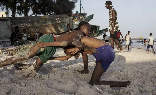 Youths wrestle on the beach in Thiaroye-Sur-Mer, Senegal, Friday, Aug. 23, 2024. Migrants leave on artisanal fishing boats known as pirogues and navigate for several days against strong winds and Atlantic currents. While thousands have survived the risky journey, many die or disappear along the way with remains sometimes washing up on the other side of the Atlantic. (AP Photo/Annika Hammerschlag)