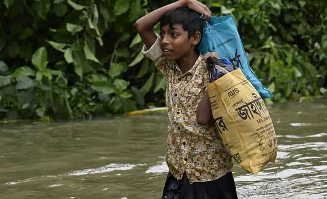 A boy carries his belongings to a temporary shelter through a flooded street in Feni, a coastal district in southeast Bangladesh, Friday, Aug. 23, 2024. (AP Photo/Fatima Tuj Johora)