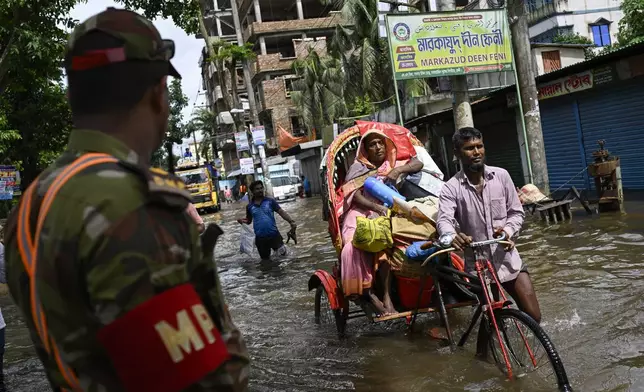 A Bangladeshi army soldier watches as people carrying their belongings wade through flooded water to reach a relief center in Feni, a coastal district in southeast Bangladesh, Friday, Aug. 23, 2024. (AP Photo/Fatima Tuj Johora)