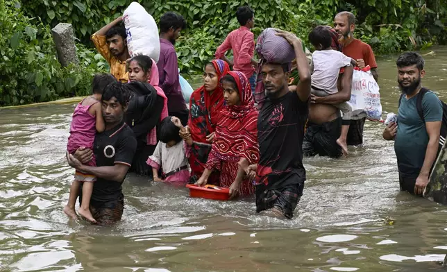 People carry their belongings and wade through flooded water to reach a temporary shelter in Feni, a coastal district in southeast Bangladesh, Friday, Aug. 23, 2024. (AP Photo/Fatima Tuj Johora)