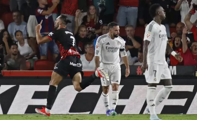 Mallorca's Vedat Muriqi, left, runs past Real Madrid's Dani Carvajal, left and Vinicius Junior while celebrating after scoring his side's first goal during a Spanish La Liga soccer match between Mallorca and Real Madrid at the Son Moix Stadium in Palma de Mallorca, Spain, Sunday, Aug. 18, 2024. (AP Photo/Francisco Ubilla)