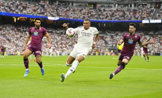 Real Madrid's Kylian Mbappe, centre, challenges for the ball with Valladolid's Eray Comert, left, and Luis Perez during the Spanish La Liga soccer match between Real Madrid and Valladolid at the Santiago Bernabeu stadium in Madrid, Spain, Sunday, Aug. 25, 2024. (AP Photo/Manu Fernandez)