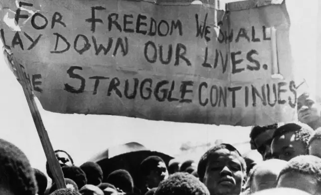 FILE- A banner is held aloft above black students in Johannesburg, South Africa, in the township of Soweto where they rallied after the funeral of a 16-year-old black student who died in jail, Oct. 18, 1976. (AP Photo)