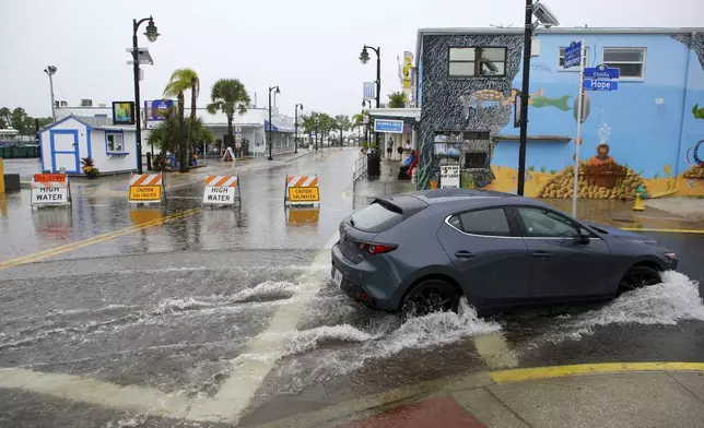 Visitors to the Tarpon Springs Sponge Docks navigate a flooded street on Sunday, Aug 4, 2024 in Tarpon Springs, Fla., as Tropical Storm Debby stirs moisture offshore in the Gulf of Mexico. (Douglas R. Clifford/Tampa Bay Times via AP)