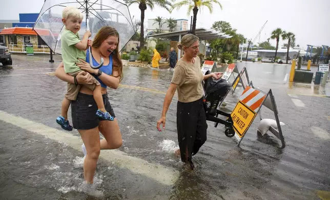 Mabrey Shaffmaster, left, carries her nephew, Arlo Hoggard, 3, left, as her sister, Morgan Hoggard, carries nine-month-old son Ace Hoggard through a flooded street as Tropical Storm Debby approaches Florida on on Sunday, Aug 4, 2024 in Tarpon Springs, Fla. (Douglas R. Clifford/Tampa Bay Times via AP)