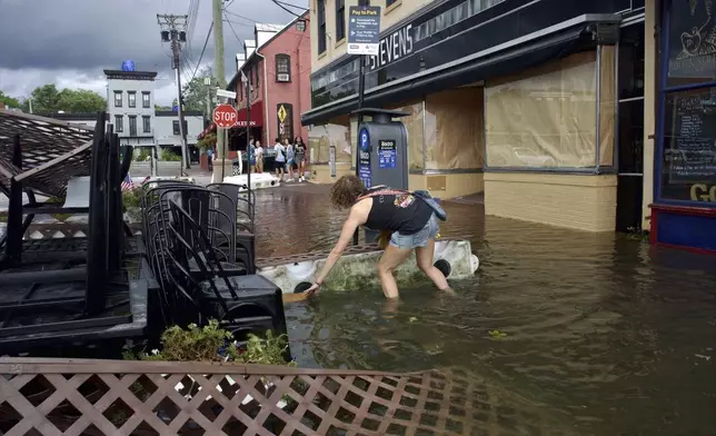 Kari Lynch pick up trash from flood waters near the City Dock in Annapolis, Md., on Friday, Aug. 9, 2024. (Kaitlin Newman/The Baltimore Banner via AP)