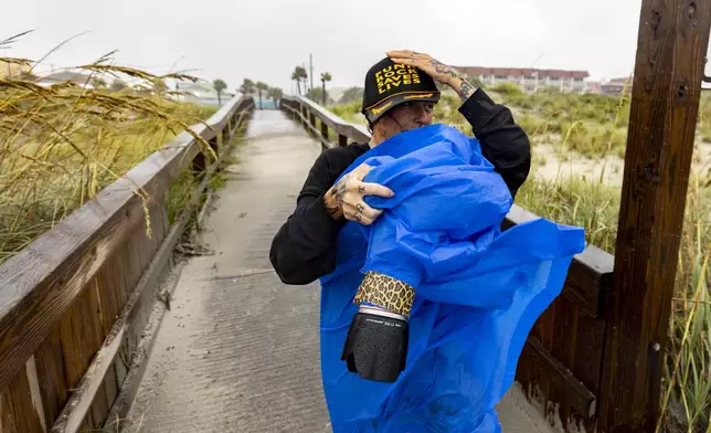 Amy Tittle holds on to her hat while trying to photograph her son surfing in the high waves created by Tropical Storm Debby near the Tybee pier, Tuesday, Aug. 6, 2024, in Tybee Island, Ga. (AP Photo/Stephen B. Morton)