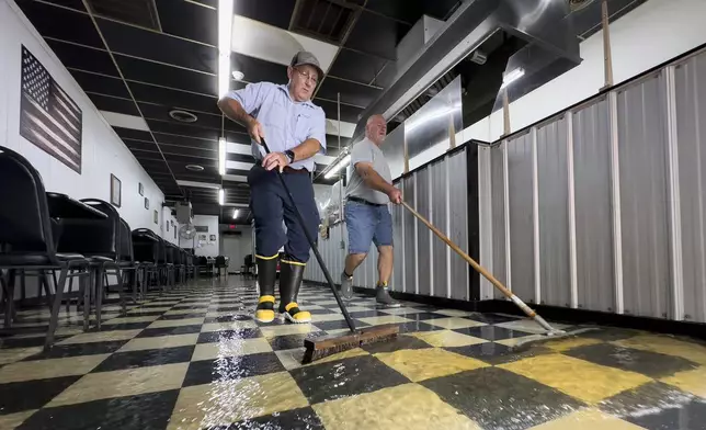 Randy Sikes, left, brooms water out of Diamond Dave's Grill as residual rain water flooding the downtown area due to Tropical Storm Debby begins to recede, Thursday, Aug. 8, 2024, in Bladenboro, NC. (AP Photo/John Minchillo)