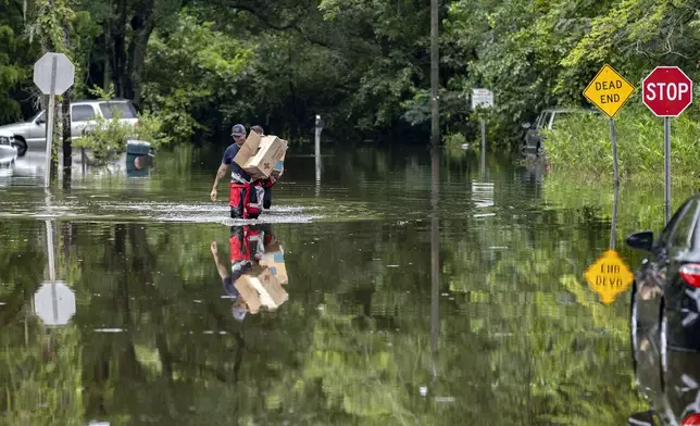 Savannah Fire Advanced Firefighters Andrew Stevenson, front, and Ron Strauss carry food to residents in the Tremont Park neighborhood that where stranded in flooding from Tropical Storm Debby, Tuesday, Aug. 6, 2024, in Savannah, Ga. (AP Photo/Stephen B. Morton)