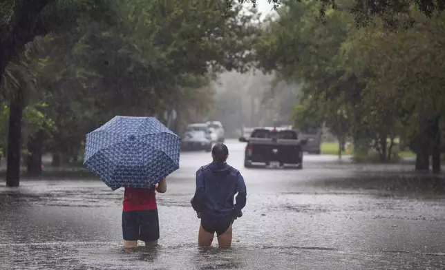 People wade into the flood waters overcoming Gordon Street as rain continues to fall from Tropical Storm Debby, Tuesday, Aug. 6, 2024, in Charleston, S.C. (Henry Taylor/The Post And Courier via AP)