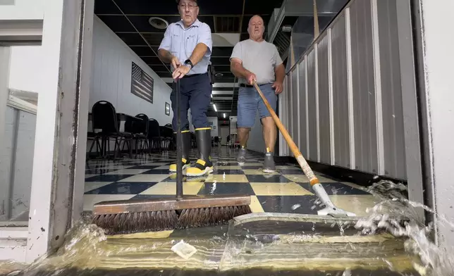 Randy Sikes, left, brooms water out of Diamond Dave's Grill as residual rain water flooding the downtown area due to Tropical Storm Debby begins to recede, Thursday, Aug. 8, 2024, in Bladenboro, NC. (AP Photo/John Minchillo)