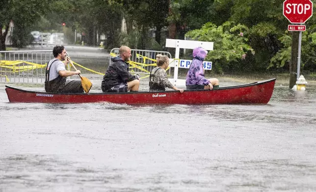 Trip Hamilton paddles his friends Brandin Gates, second from left, Mallie Taylor, second from right, and Ellie Combs, right, all from Charleston, S.C., in a canoe down Ashley Ave in Charleston as Tropical Storm Debby approaches, Tuesday, Aug. 6, 2024. (AP Photo/Mic Smith)