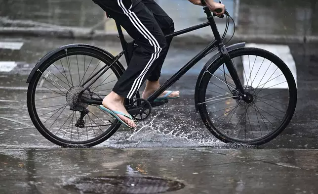 A person wears flip flops as they ride their bike through a puddle in Ottawa, Ontario, Friday, Aug. 9, 2024. (Justin Tang/The Canadian Press via AP)