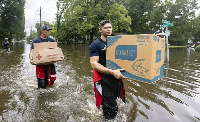 Savannah Fire Advanced Firefighters Ron Strauss, right, and Andrew Stevenson, left, carry food to residents in the Tremont Park neighborhood that where stranded in flooding from Tropical Storm Debby, Tuesday, Aug. 6, 2024, in Savannah, Ga. (AP Photo/Stephen B. Morton)