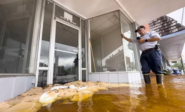 Randy Sikes speaks to his relatives on a mobile phone as he stands in residual rain water flooding the downtown area caused by Tropical Storm Debby, Thursday, Aug. 8, 2024, in Bladenboro, NC. (AP Photo/John Minchillo)