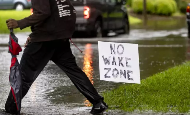 A pedestrian walks past a sign on a flooded street after heavy rain from Tropical Storm Debby, Monday, Aug. 5, 2024, in Savannah, Ga. (AP Photo/Stephen B. Morton)