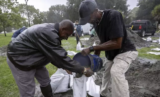 Hershey Stepherson, left, and Bryan Burc, right, use a five gallon bucket to fill a sandbag while preparing for Hurricane Debby, Monday, Aug. 5, 2024, in Savannah, Ga. Debby reached the Big Bend coast of Florida early Monday, bringing with it the potential for catastrophic flooding and life-threatening storm surge. (AP Photo/Stephen B. Morton)