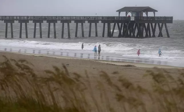 Beach goers walk near the Tybee pier as wind and rain from Tropical Storm Debby start to come ashore, Monday, Aug. 5, 2024, in Tybee Island, Ga. (AP Photo/Stephen B. Morton)