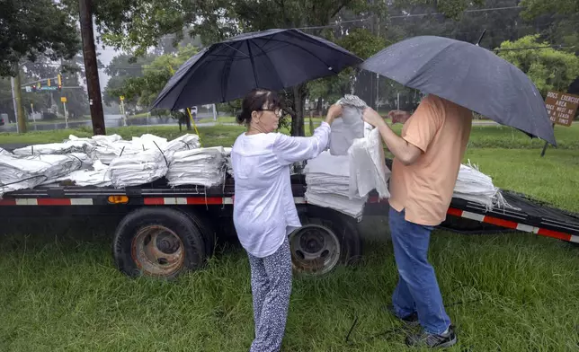 Angela Ortiz, left, hands her son Barrett Ortiz, right a stack of sandbags while preparing for Hurricane Debby at a county park, Monday, Aug. 5, 2024, in Savannah, Ga. Debby reached the Big Bend coast of Florida early Monday, bringing with it the potential for catastrophic flooding and life-threatening storm surge. (AP Photo/Stephen B. Morton)