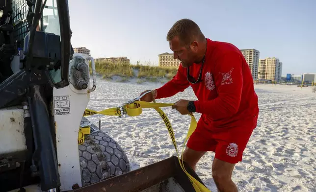 Patrick Brafford, a beach lifeguard manager, uses a tie down strap to help secure a compact track loader and a lifeguard tower to help pull it further away from the water in preparation of potential storm at Clearwater Beach on Saturday, Aug. 3, 2024, in Clearwater, Fla. (Jefferee Woo/Tampa Bay Times via AP)