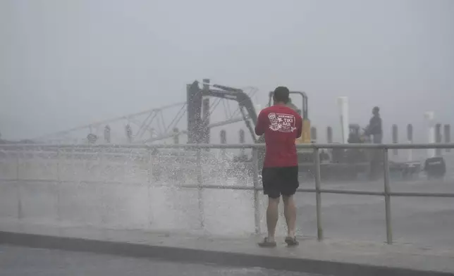 A man takes photos of a construction crew attempting to remove equipment as surf pushed by winds from Tropical Storm Debby break over the sea wall in Cedar Key, Fla., on Sunday, Aug. 4, 2024. (AP Photo/Christopher O'Meara)