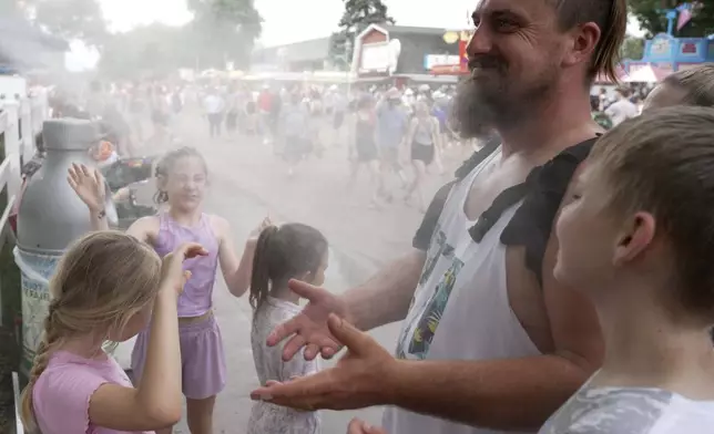 Seven-year-old Harper Perkins, center, and her sister Brielle, of Princeton, Minn., cool off in a misting fountain at the Minnesota State Fair in Falcon Heights, Minn., on Monday, Aug. 26, 2024. (AP Photo/Mark Vancleave)