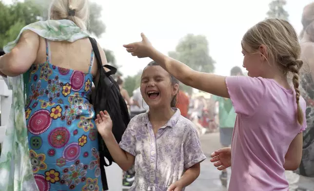 Seven-year-old Harper Perkins, center, and her sister Brielle of Princeton, Minn., cool off in a misting fountain at the Minnesota State Fair in Falcon Heights, Minn., on Monday, Aug. 26, 2024. (AP Photo/Mark Vancleave)