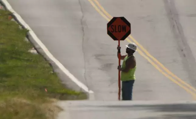 A worker is diffused by heat vapors while directing traffic around a construction project as temperatures topped 100 degrees Fahrenheit (37.8 Celsius) on Monday, Aug. 26, 2024, in Olathe, Kan. (AP Photo/Charlie Riedel)