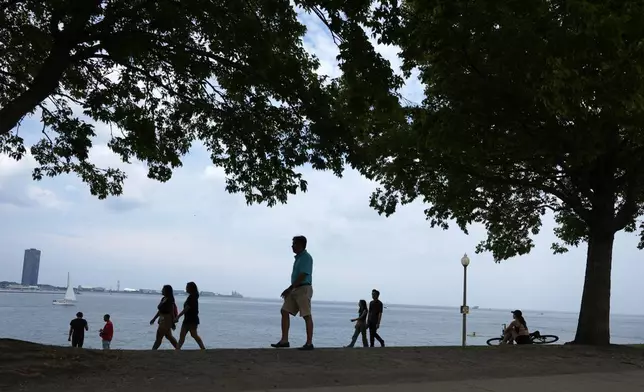 A cyclists, right, sits under the shade of a tree as others walk along Lake Michigan on Tuesday, Aug. 27, 2024, as a second straight day of hot soupy temperatures approaching triple digits hung over much of the Midwest on Tuesday, in Chicago. (AP Photo/Charles Rex Arbogast)