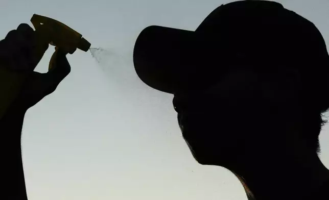 John Nguyen sprays water to cool off after shooting hoops during a hot weather day in Deerfield, Ill., Monday, Aug. 26, 2024. (AP Photo/Nam Y. Huh)