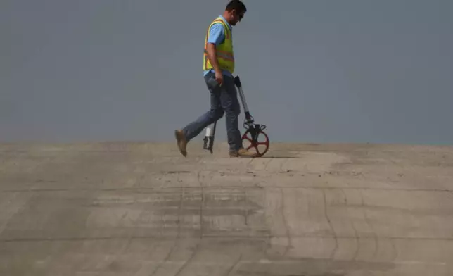 A worker is diffused by heat vapors while marking pavement on a street construction project as temperatures topped 100 degrees Fahrenheit (37.8 Celsius) on Monday, Aug. 26, 2024, in Lenexa, Kan. (AP Photo/Charlie Riedel)