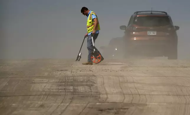 A worker is diffused by heat vapors while marking pavement on a street construction project as temperatures topped 100 degrees Fahrenheit (37.8 Celsius) on Monday, Aug. 26, 2024, in Lenexa, Kan. (AP Photo/Charlie Riedel)