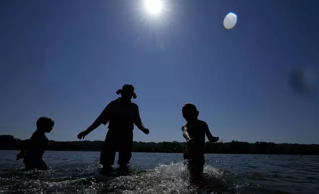 Bob Boyle, center, of Des Moines, Iowa, stands in the water with his grandchildren Abby, left, and Judah Boyle at Gray's Lake Park, Monday, Aug. 26, 2024, in Des Moines, Iowa. (AP Photo/Charlie Neibergall)