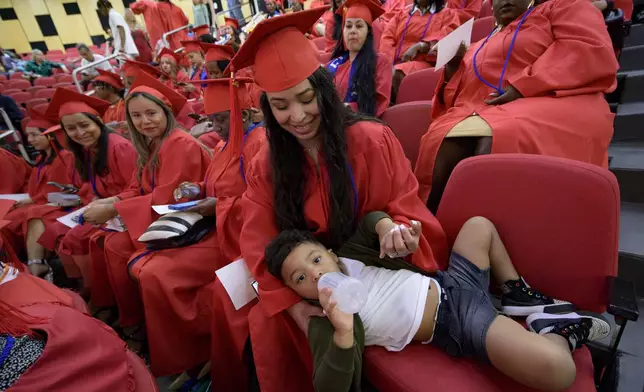 Litzy Moreno helps her son, Liam Ayala, 2, with a bottle before receiving her high school equivalency (HiSET) diploma during a graduation ceremony for the Youth Empowerment Project (YEP) in New Orleans, Thursday, June 27, 2024. YEP is a New Orleans-based non-profit organization which received money from the NBA Foundation program. (AP Photo/Matthew Hinton)