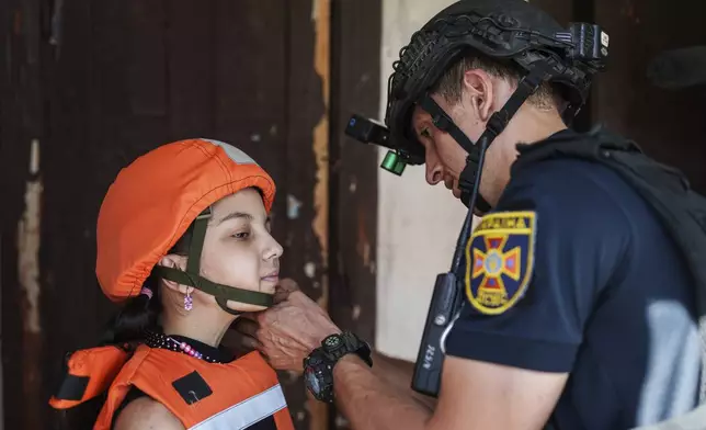 A Fenix team rescue worker places a helmet on a girl during the evacuation of local population to safe areas, in Selidove, Donetsk region, Ukraine, on Tuesday, August 20, 2024. (AP Photo/Evgeniy Maloletka)