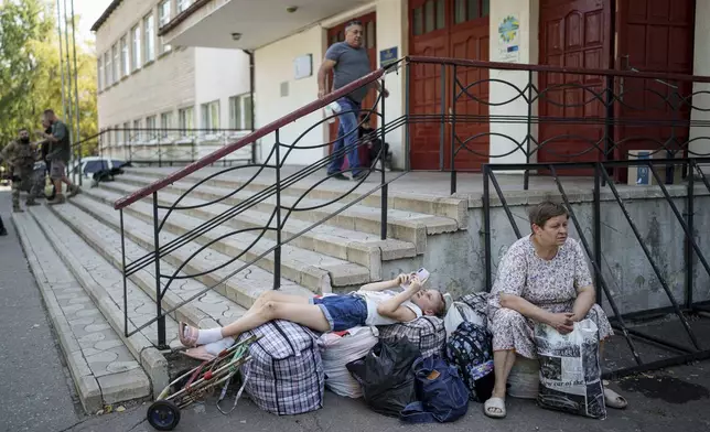 Tetiana, 11, lays on their possessions as she and her grandmother Tetiana, 61, wait for transfer to the train station during the evacuation of local people from Selidove to safe areas, in Pokrovsk, Donetsk region, Ukraine, on Tuesday, Aug. 20, 2024. (AP Photo/Evgeniy Maloletka)