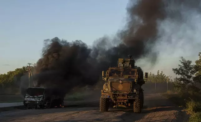 A Ukrainian armoured military vehicle travels past a burned car near the Russian-Ukrainian border, Sumy region, Ukraine, Wednesday, Aug. 14, 2024. (AP Photo/Evgeniy Maloletka)