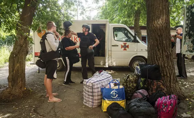 A Fenix team rescue worker places a helmet on Maryna Scherbyna as she and her children are evacuated as local people are moved from Selidove to safe areas, in Pokrovsk, Donetsk region, Ukraine, on Tuesday, Aug. 20, 2024. (AP Photo/Evgeniy Maloletka)