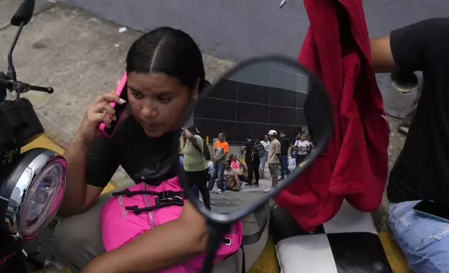 A woman sits outside the Boleita National Police detention center after her boyfriend was arrested during recent opposition protests against the official results of the presidential election in Caracas, Venezuela, Thursday, Aug. 1, 2024. The line reflected in the motorcycle mirror is of relatives of other detainees also arrested during protests. (AP Photo/Matias Delacroix)