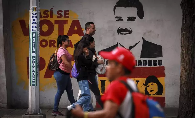 Pedestrians walk past a campaign mural featuring President Nicolas Maduro, in Caracas, Venezuela, Friday, Aug. 2, 2024. (AP Photo/Bernardo Suarez)