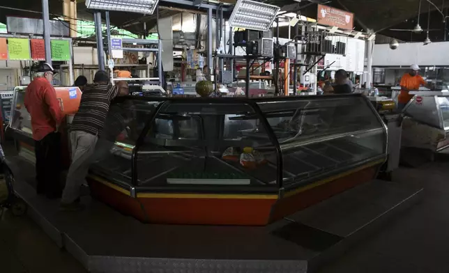 Vendors stand next to dark, empty refrigerators at a markek in Valencia, Venezuela, Friday, Aug. 30, 2024, during a blackout that affected most of the country. (AP Photo/Jacinto Olivares)