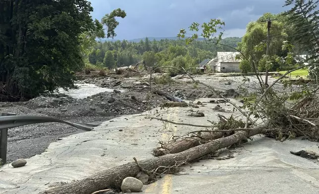 Trees sit across a roadway destroyed by flash floods in Lyndonville, Vt., Wednesday, July 31, 2024. Parts of the state hit by flooding Monday night and Tuesday are bracing again as a new round of severe thunderstorms moves through the region. (AP Photo/Nick Perry)