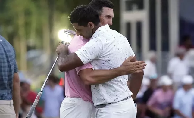 Aaron Rai, of England, front, is hugged by playing partner Billy Horschel, back, after winning the Wyndham Championship golf tournament in Greensboro, N.C., Sunday, Aug. 11, 2024. (AP Photo/Chuck Burton)