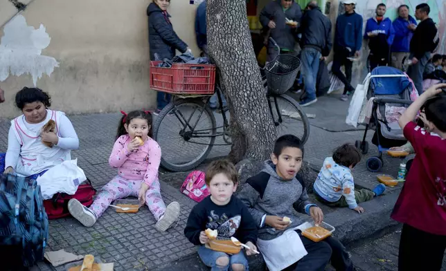 Children eat a free, cooked meal outside a soup kitchen on the outskirts of Buenos Aires, Argentina, Thursday, Sept. 12, 2024. (AP Photo/Natacha Pisarenko)