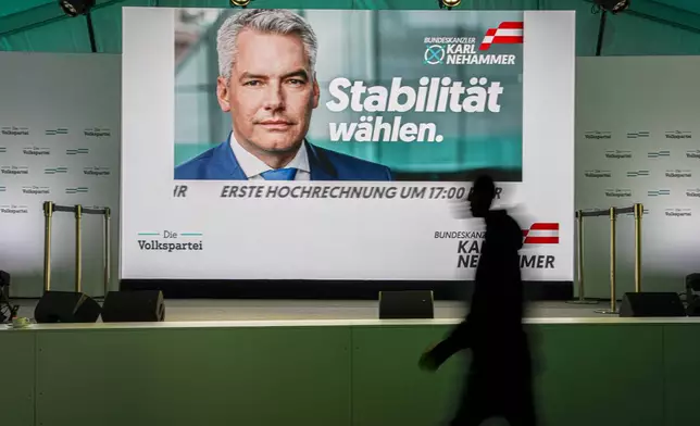 A person walks by a display showing electoral visuals of Austrian Chancellor Karl Nehammer at the OVP, Austrian People's Party, headquarters in Vienna, Austria, Sunday, Sept. 29, 2024. (AP Photo/Andreea Alexandru)