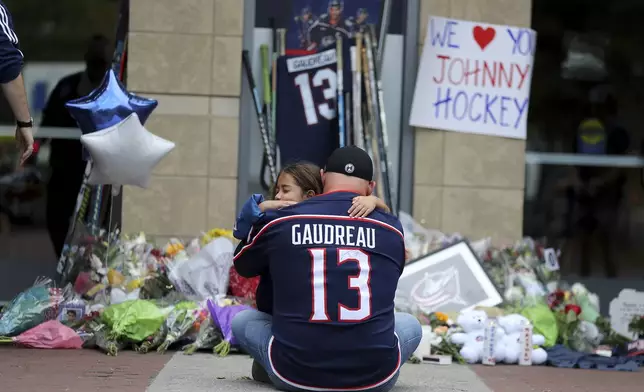 Shiloh Rivera, facing, mourns with Hylas Stemen of Columbus, at the makeshift memorial set up by fans for Blue Jackets hockey player Johnny Gaudreau in Columbus, Ohio, Friday, Aug. 30, 2024. Gaudreau, along with his brother Matthew, was fatally struck by a motorist while riding his bicycle on Thursday. (AP Photo/Joe Maiorana)