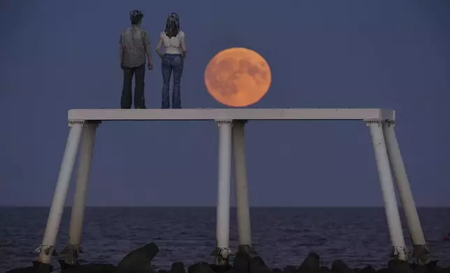 The full Harvest moon rises over 'The Couple' sculpture at Newbiggin-by-the-Sea in Northumberland, Tuesday Sept. 17, 2024. (Owen Humphreys/PA via AP)