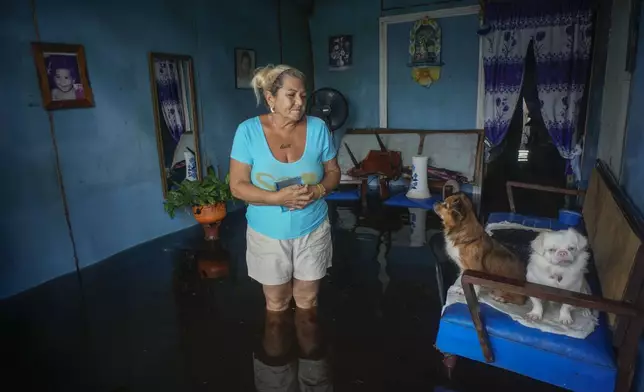 A woman looks at her dogs sitting on a sofa, as she stands inside her home that was flooded in the passing of Hurricane Helene, in Batabano, Mayabeque province, Cuba, Thursday, Sept. 26, 2024. (AP Photo/Ramon Espinosa)