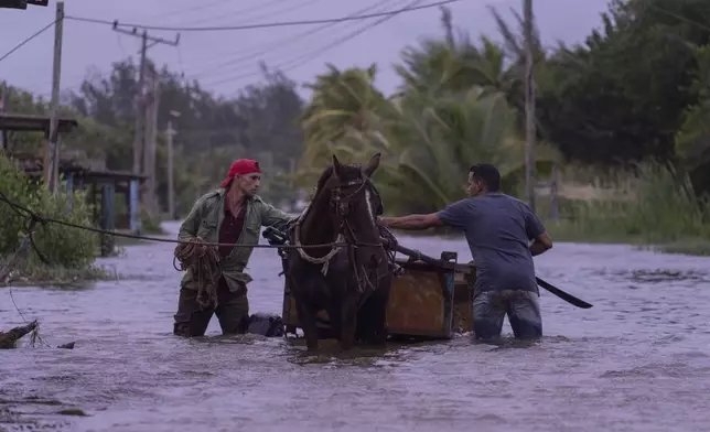 People traverse a flooded street with a horse-drawn carriage after the passage of Hurricane Helene in Guanimar, Artemisa province, Cuba, Wednesday, Sept. 25, 2024. (AP Photo/Ramon Espinosa)